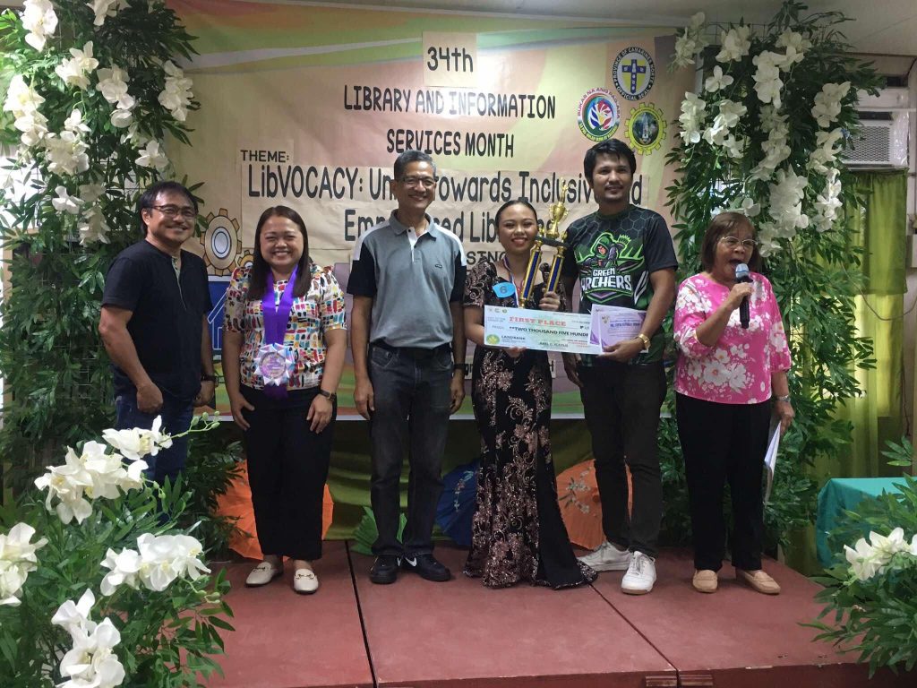 Maria Lucia Fatima, grade 9 of Moreno Integrated HS who bagged first place in Kundiman Singing Contest receives trophy and cash prize of P2,500 during the awarding ceremony of the 34th Library and Information Services Month in Camarines Norte. Beside her (left) is Museum Curator Abel Icatlo, OIC of LIS and coaches.